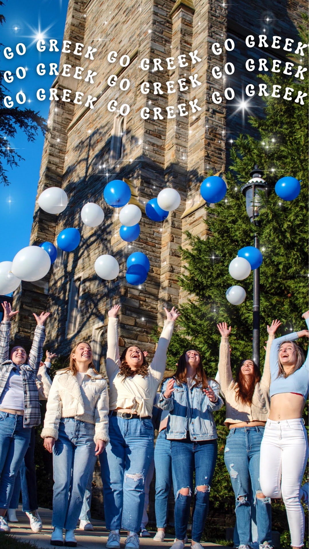 Color photo. There are seven women at the bottom of the photo, dressed in blues and lighter colors. They have thrown blue and white balloons in the air, and are smiling with their arms in the air as they watch the balloons they have thrown. In the background are green trees, a clear sky, and Barbelin hall at Saint Joseph's University.  There is white text at the top of the photo that repeatedly states “go greek,” with white sparkles surrounding the letters. 